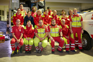 Gruppe von Rettungskräften in roten und gelben Uniformen, lachend und posierend.