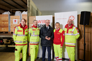 Fünf Personen in Arbeitskleidung stehen vor einem Lkw mit Spendenboxen.